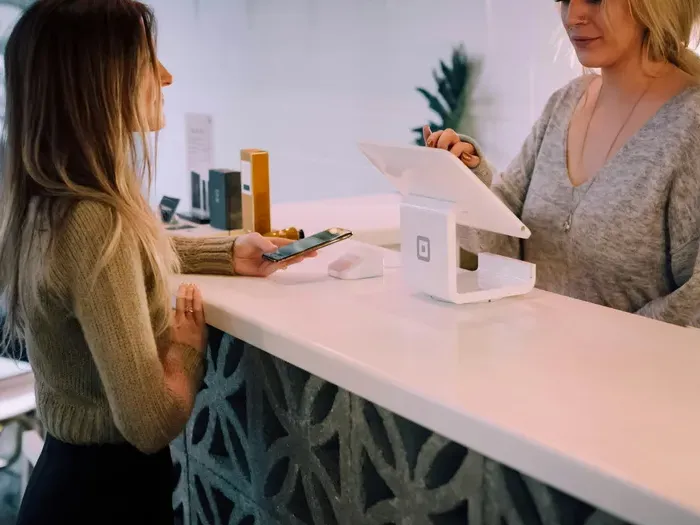 Customer paying at a shop counter with smartphone while staff assists, highlighting vendors on Local Directory 360